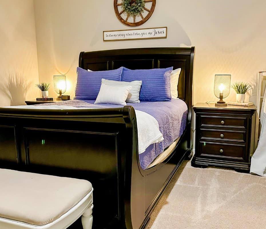 black sleigh bed with blue comforter and pillows. black night stand beside the bed with a black up lamp and faux plant on top. home decorating is hard