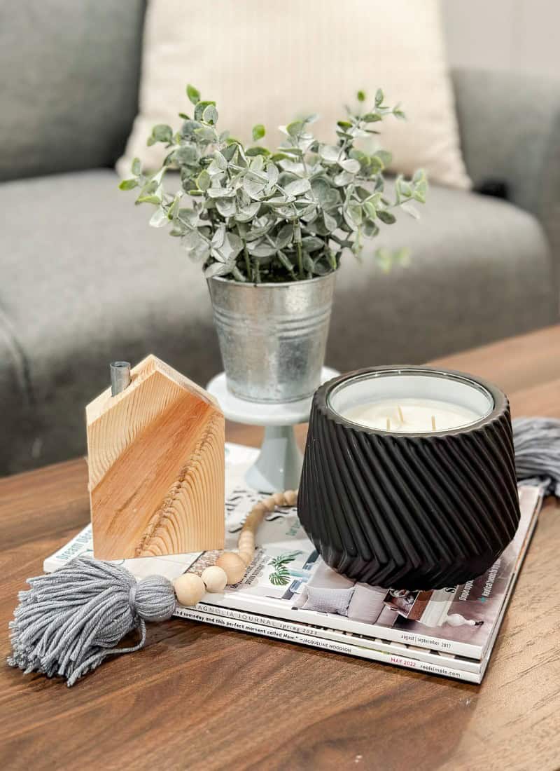 decorating is hard feature black candle , wood beads, a wood house cutout and faux eucalyptus plant on a stack of magazines