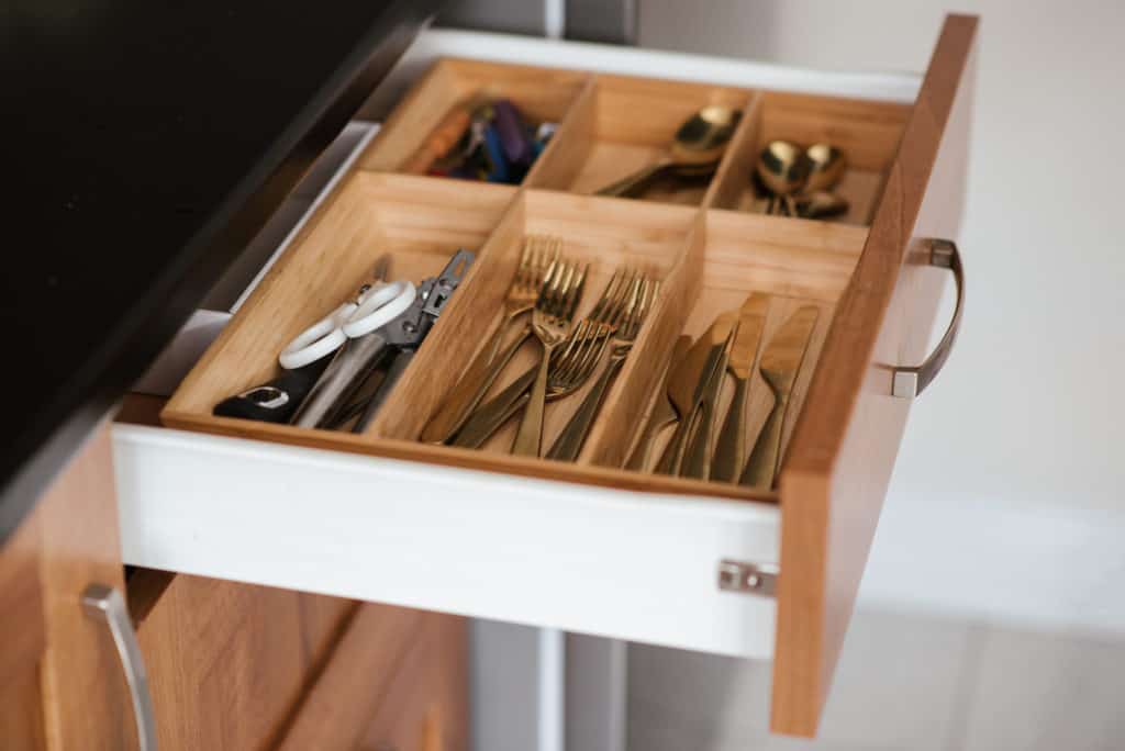 An organized silverware drawer is an important part of Kitchen organization. this drawer picture features 6 wooden compartments each containing gold forks, knives, spoons and other kitchen gadgets.
