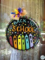 Back To School Wreath made out of a round pizza pan painted black with red, orange, yellow, green, blue and purple crayon shapes. large colorful bow and polka dots all over.