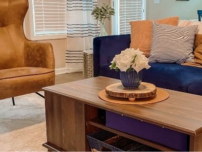 Navy blue couch with pink pillow, white flowers in blue vase on brown coffee table. brown leather chair to left.