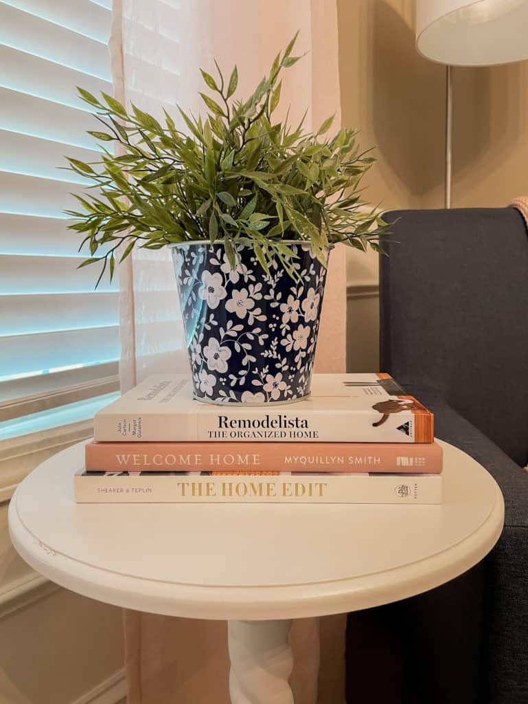 Blue and white planter with green plant on top of 3 books on round white table.