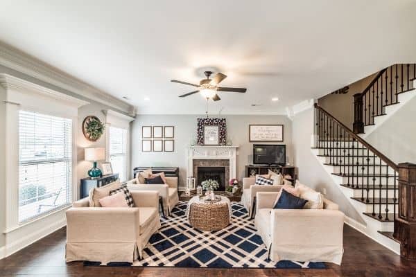 living room with 4 light colored chairs on a navy rug with round wicker coffee table. fire place, Television and piano on back wall.