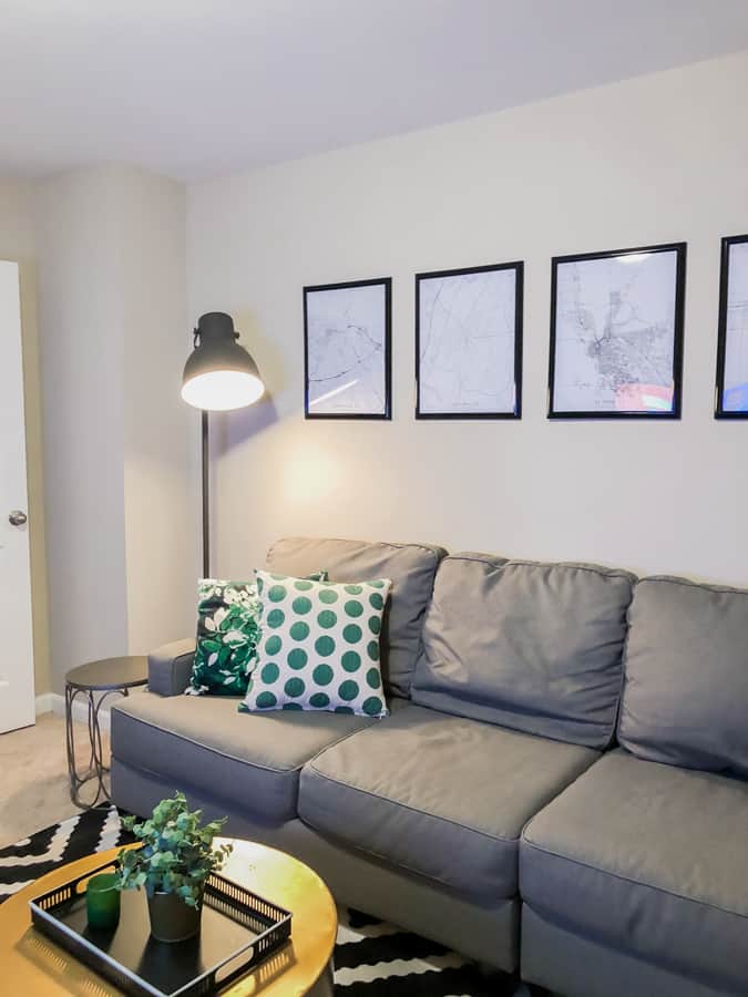 cottage keeping grey couch with green and white pillows. black and white artwork on the walls black ikea lamp in the back.
