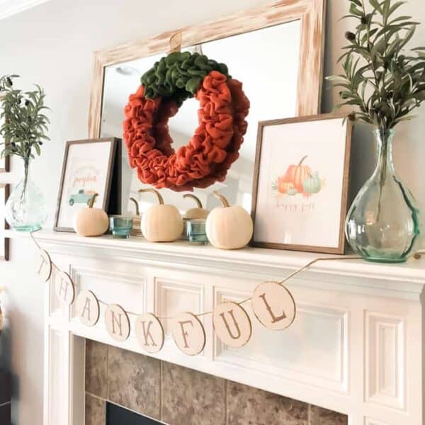 Fall mantel with mirror, orange burlap wreath, white pumpkins and framed fall prints.