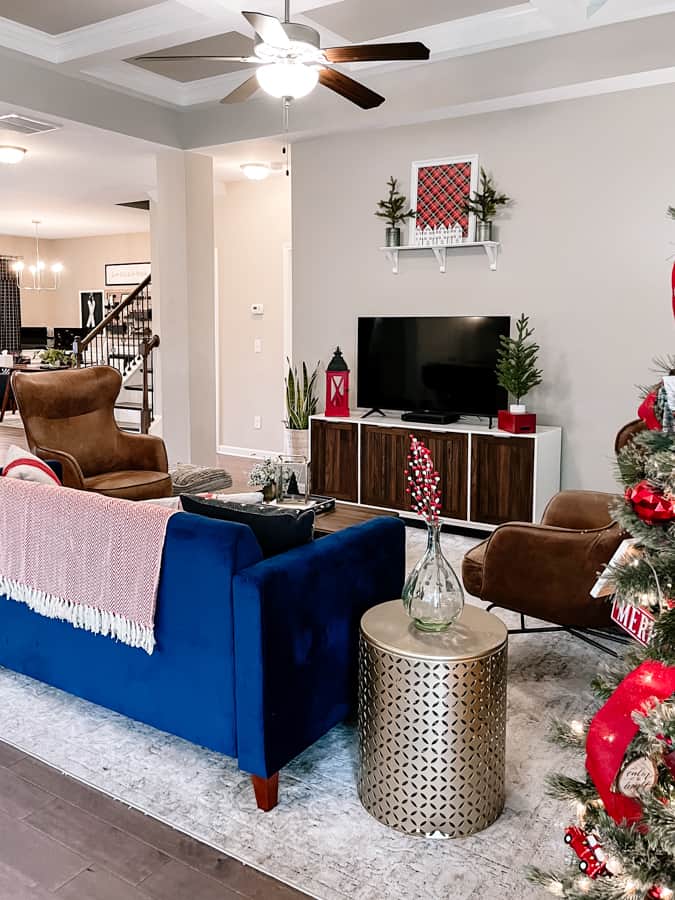 Cozy christmas living room with navy blue velvet couch, gold end table, television on white and wood tv stand. red christmas decor accents on tables