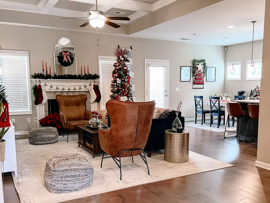 Cozy christmas living room with navy blue velvet couch, gold end table, television on white and wood tv stand. red christmas decor accents on tables. brown leather chair in front of fireplace.