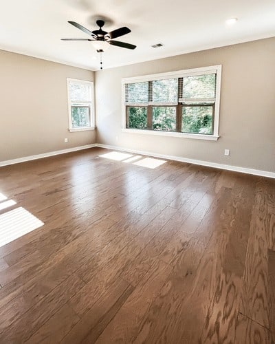 master bedroom with wood floors, grey walls and white ceiling. features 3 large windows on far wall.
