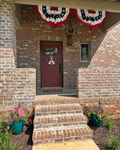 patriotic holiday decor for front porch. red white and blue bunting on top. red and blue door mat. red white and blue wreath on door.