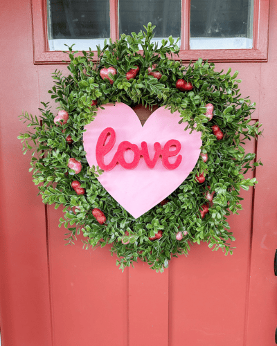 Red door with a green boxwood wreath with a pink heart and love written in red cursive letters. Easy Valentine's Day Decorations