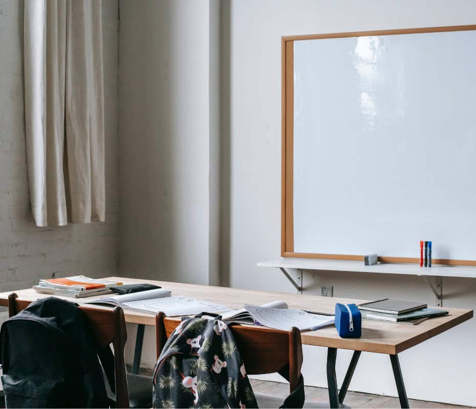 back to school classroom with whiteboard, a desk with 2 chairs. a backpack hangs on each chair. back to school success tips