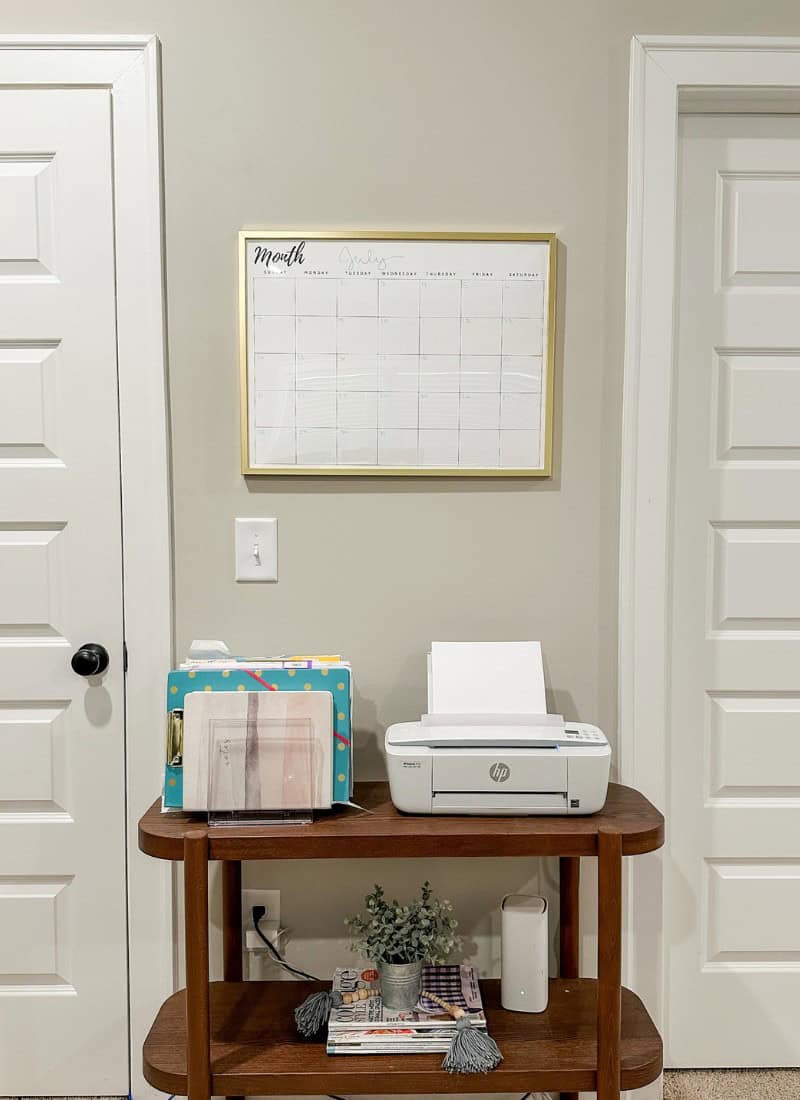 large wall calendar with gold frame hanging on a grey wall with a table underneath that has a printer and file holder. diy wall calendar