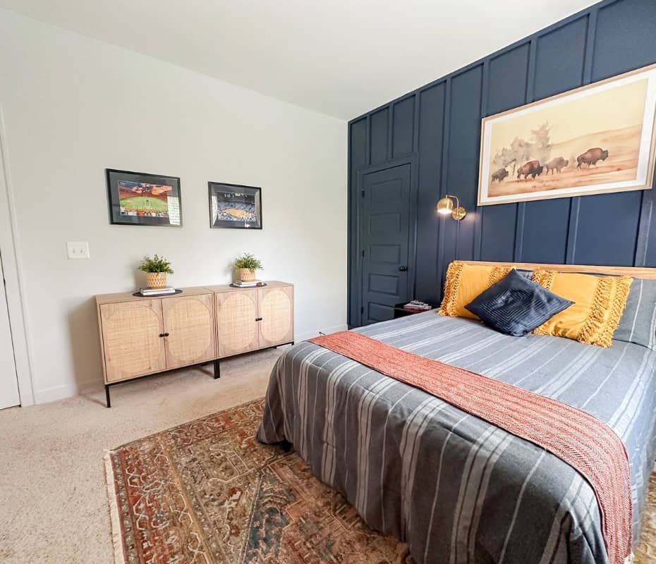 bedroom decor idea. light grey wall with light wood cabinet. yellow plant holders on top. navy blue accent wall with full size bed blue and white striped bedding