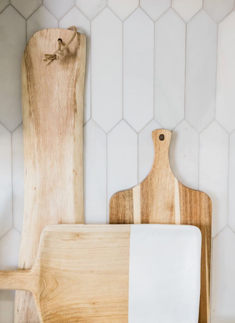 3 different size bread boards leaning against a white tile backsplash behind a stove top.