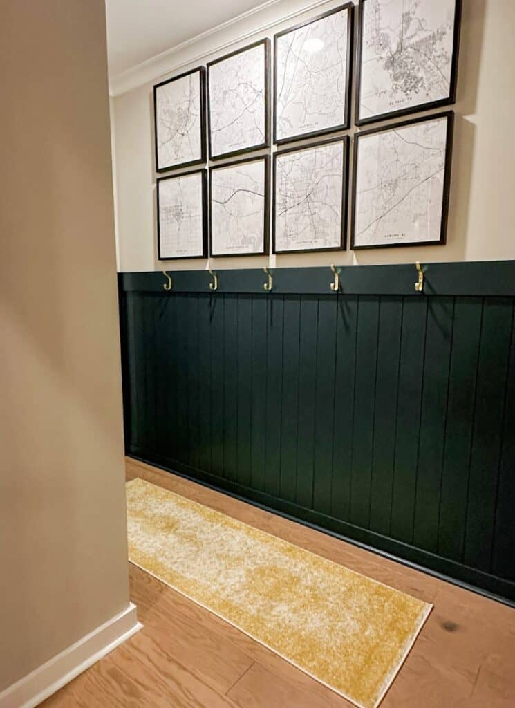 gold wall hooks in a hallway for hanging backpacks. black and white city art prints in black frames above a green half wall with vertical shiplap