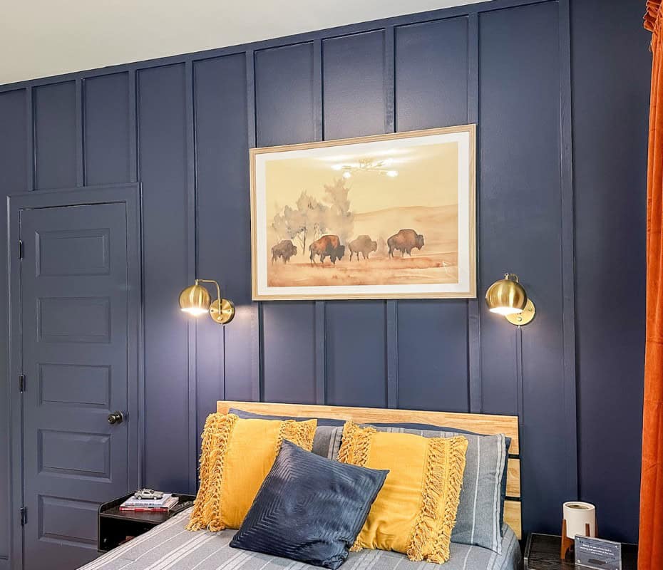 hide light cords on a blue wall. blue wall with 2 gold wall sconces over a bed. a large buffalo print is hanging between the wall sconces.