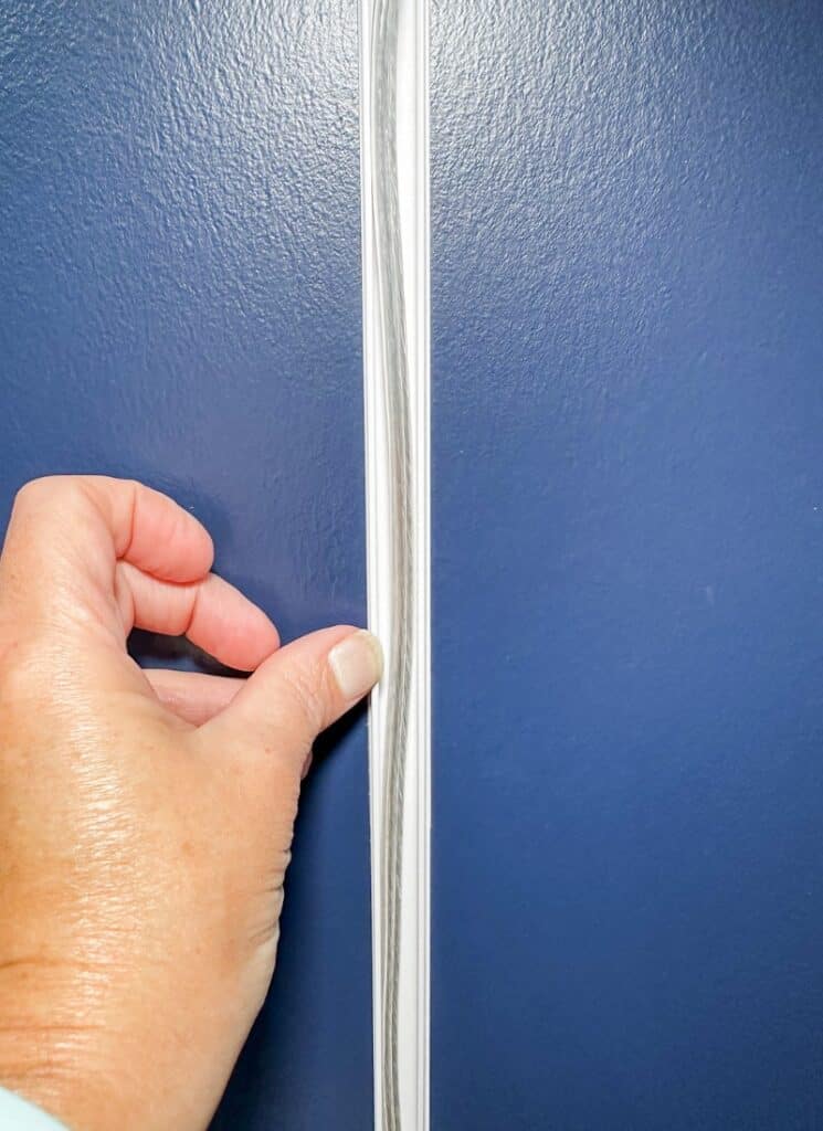 blue wall with thumb holding a cord cover track against a wall.