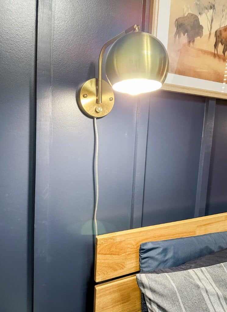 gold wall sconce on navy blue wall. uncovered light cord hanging below.