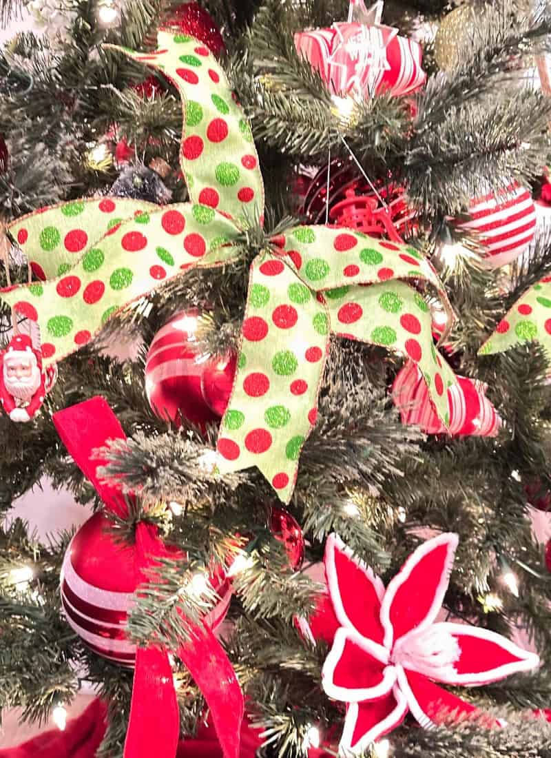 Christmas Cheer in red and green polka dot ribbon other red and white ornaments hung on a green Christmas tree