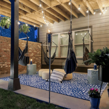 covered porch decorating idea with grey hanging swings, blue rugs and hanging white lights.